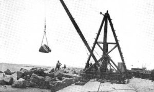 G-5925.1FF3-3 THE GALVESTON SEAWALL."  "DERRICK LAYING RIPRAP.  A1500 LB. ROCK IN MIDAIR.