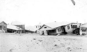 G-17713FF9.3-9 Row of wrecked houses partially submerged in sand.