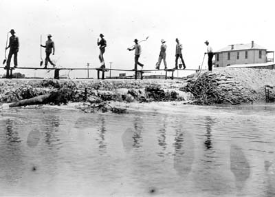 Grade Raising, Photograph of workmen crossing walkway over area being filled 