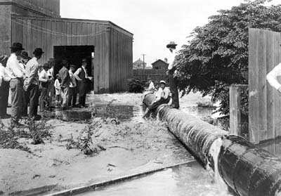 Grade Raising, Photograph of several boys seated and a man standing on pipeline discharging fill 