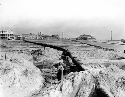 Grade Raising, Photograph of workman standing in trench next to pipeline
