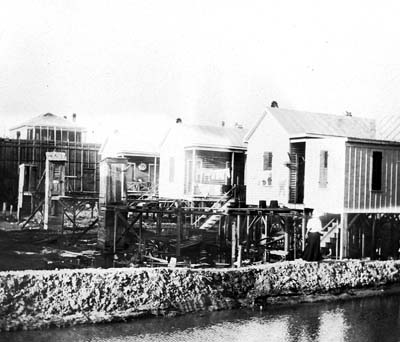 Photograph of woman and child walking on embankment past raised houses awaiting fill 