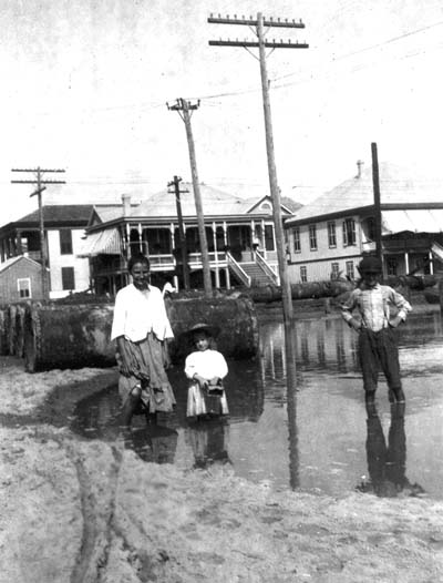 Photograph of woman, girl, and boy standing in flooded residential street 