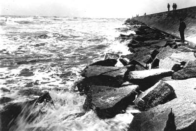 Seawall, Photograph of people standing and watching waves crash against riprap