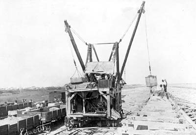 Photograph of steam mixer pouring concrete into wood caissons along beach 