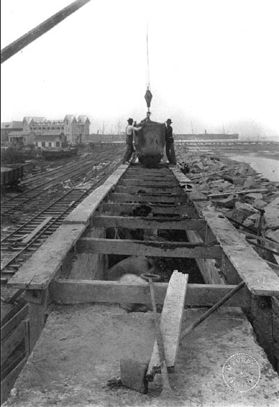 Photograph of workmen pouring concrete from steam mixer into wood caisson 