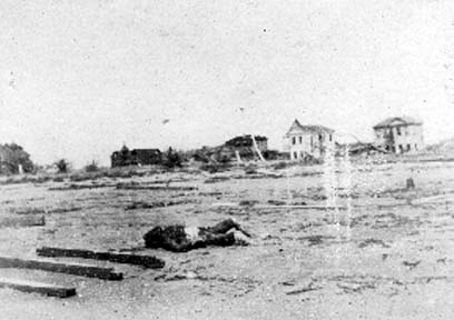 Photograph of body and wrecked houses