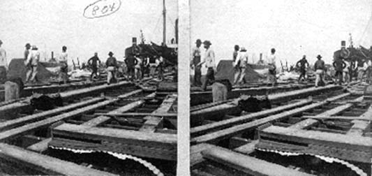 Stereo card of workers carrying body aboard barge