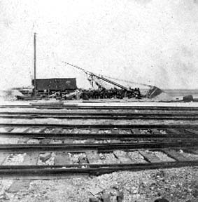 Photograph of railroad tracks, wrecked freight car and sailing vessel