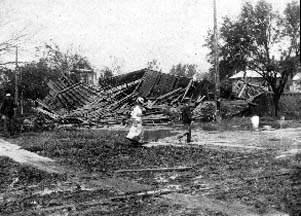 Photograph of man and woman walking past collapsed house