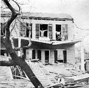 Photograph of a man standing in second-story window of a damaged house