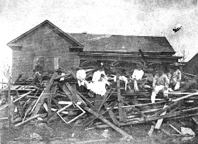 Photograph of survivors seated atop debris in front of damaged house
