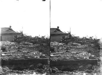 Stereo glass negative of a pile of debris surrounding damaged house