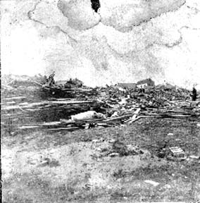 Photograph labeled Wreckage and debris near beach with body of a woman in front