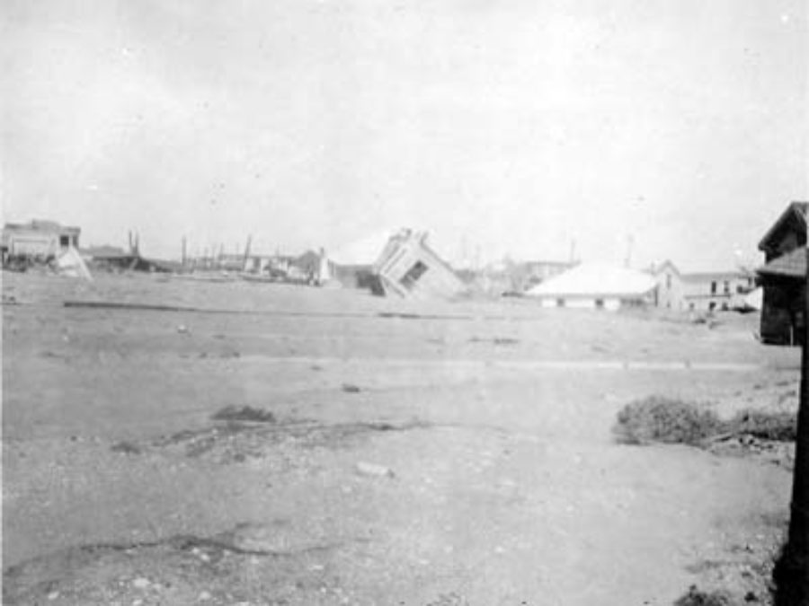 G-17713FF9.2-13 Wrecked and toppled houses partially submerged in sand