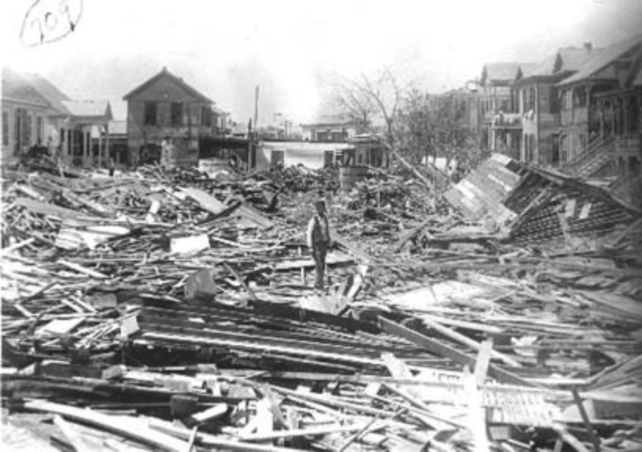G-1771FF7.3-13 Worker standing amid debris, with wrecked houses.